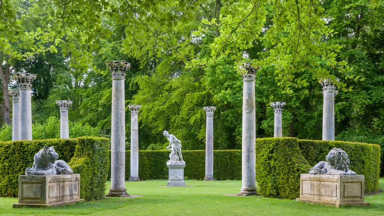 Ten Corinthian columns in a circle and lead figures of a lion and lioness. A leafy green lawn.